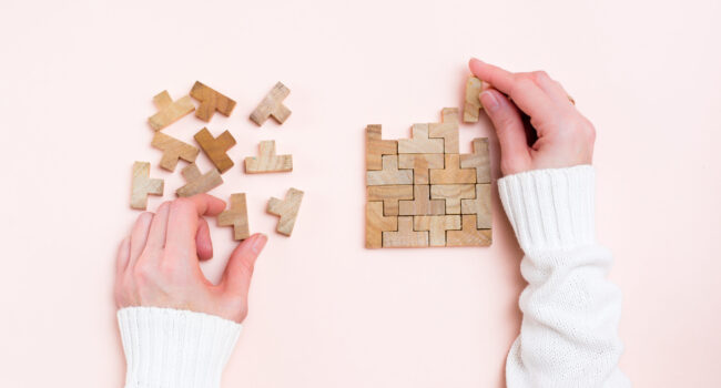 Organization and order. Female hands lay out wooden puzzle pieces on a pink background. Top view